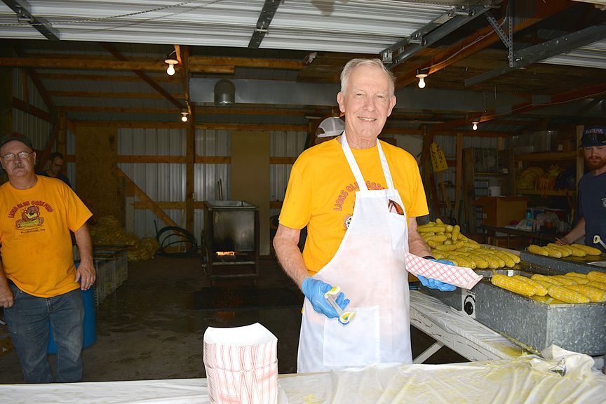 Volunteer in yellow shirt and white apron stands by tables of produce in a warehouse.