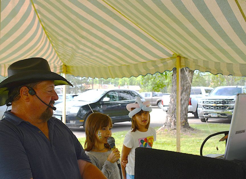 Two children and a man under a striped canopy, with cars parked in the background.