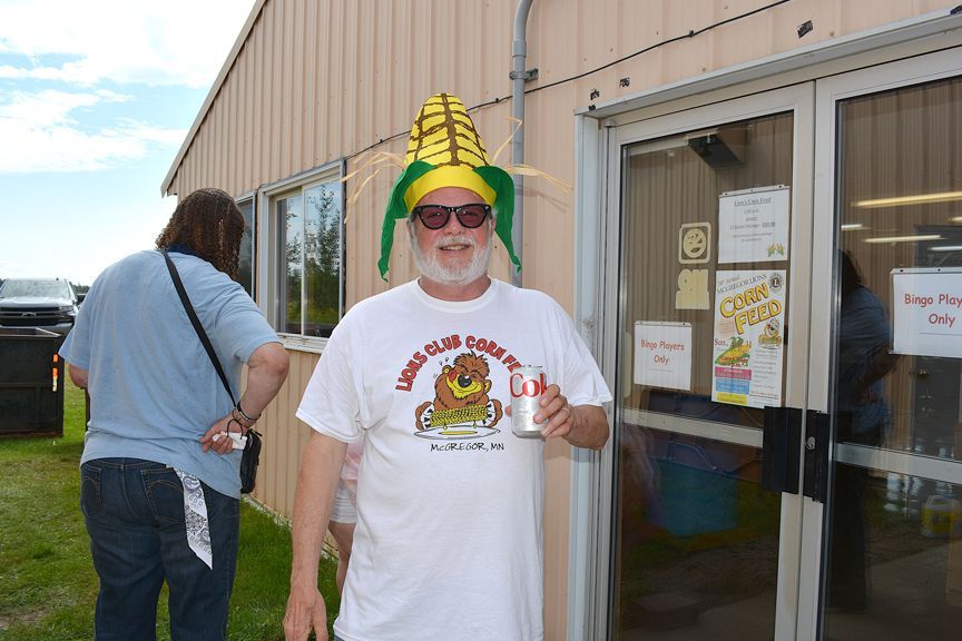 Person in a yellow hat stands smiling outside a building, holding a drink near the entrance.