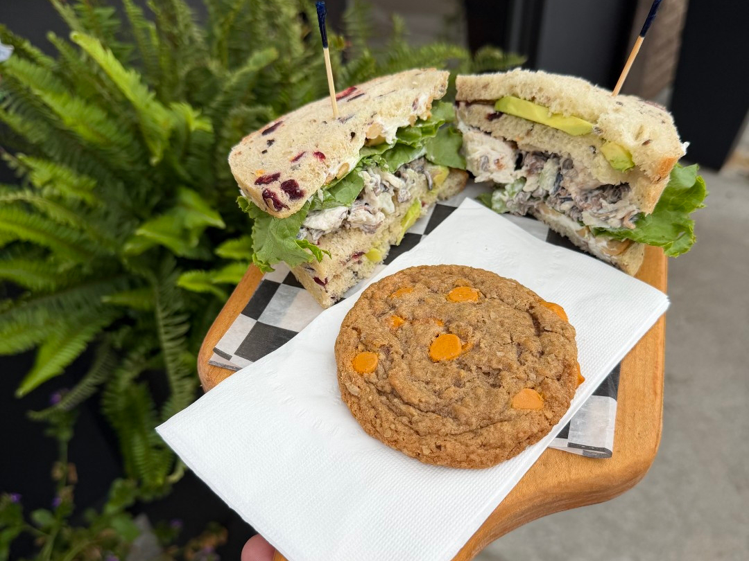 Wild rice chicken salad sandwich and cookie on a napkin atop a wooden tray