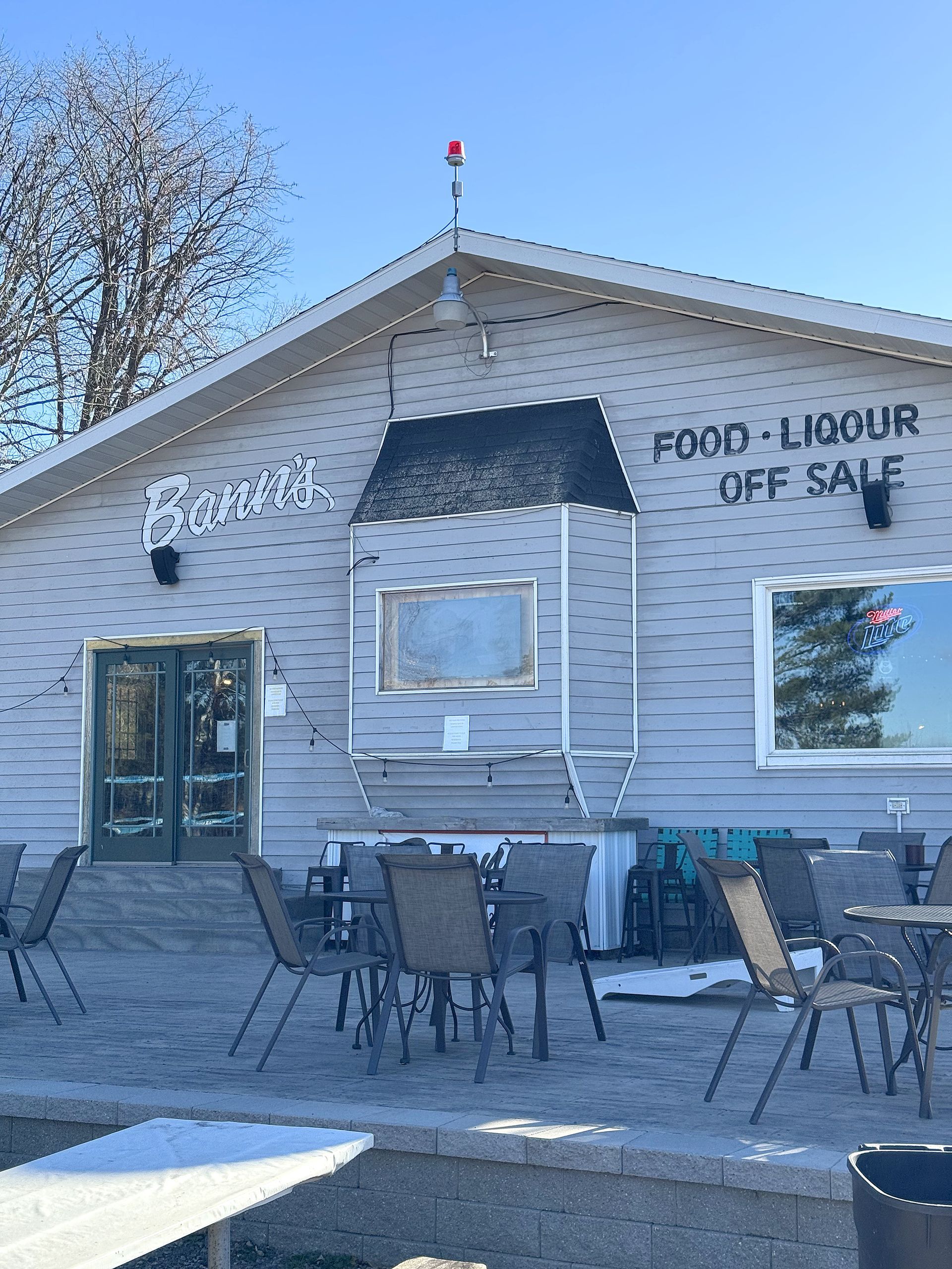 Gray building labeled “Food-Laboour Gift Cafe” with outdoor tables and chairs on a sunny day