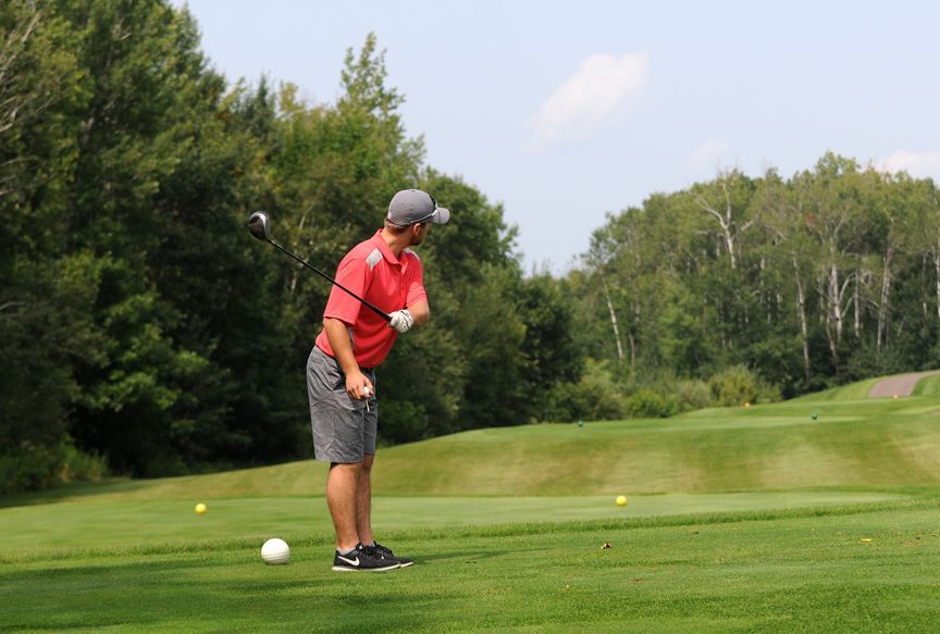Golfer in red shirt lining up a shot on a green course with trees in the background
