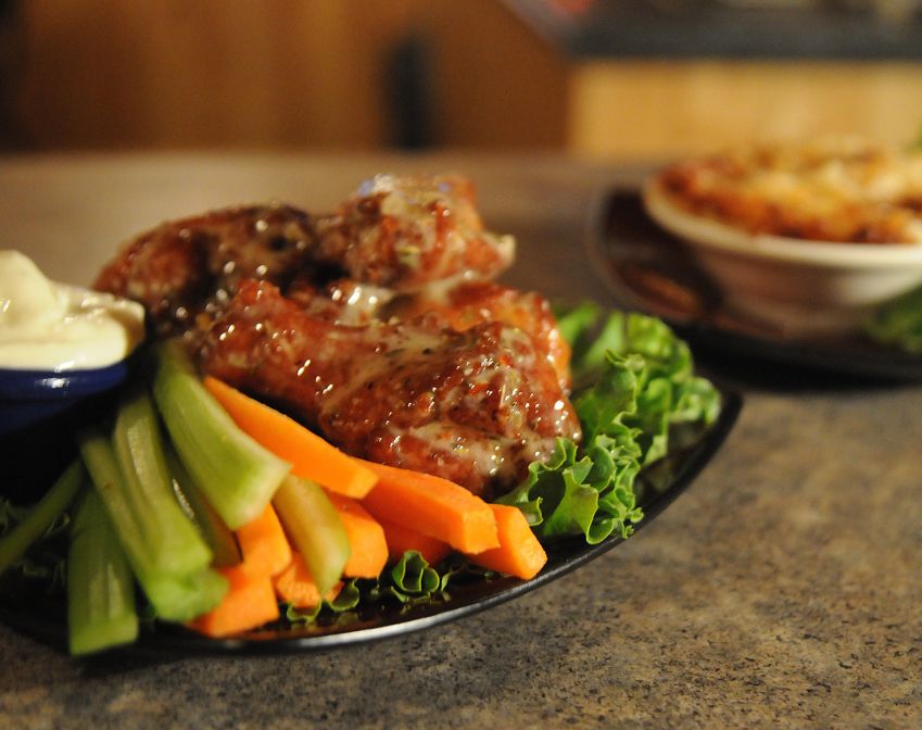 Grilled chicken with carrots and celery on a plate, with dipping sauce in a dimly lit restaurant setting