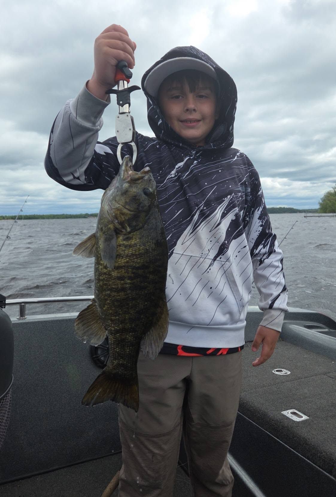 Person on a boat holding up a large fish by the line on a cloudy day.