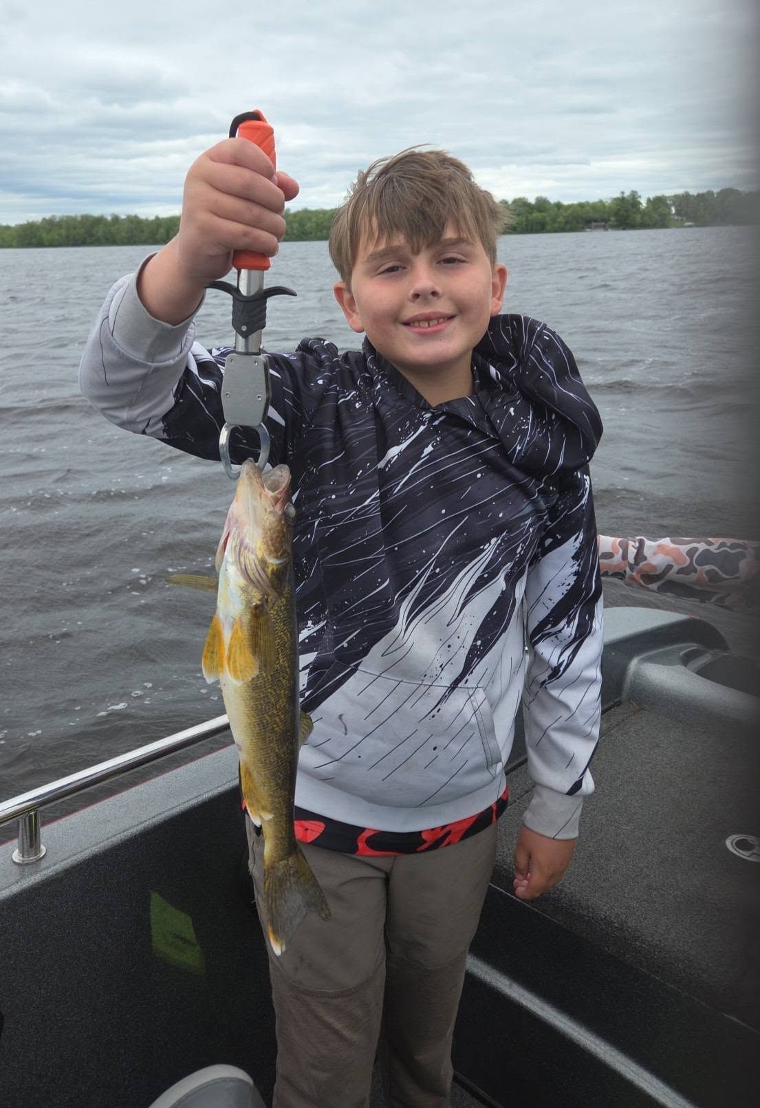 Child on a boat holding up a caught fish on a lake