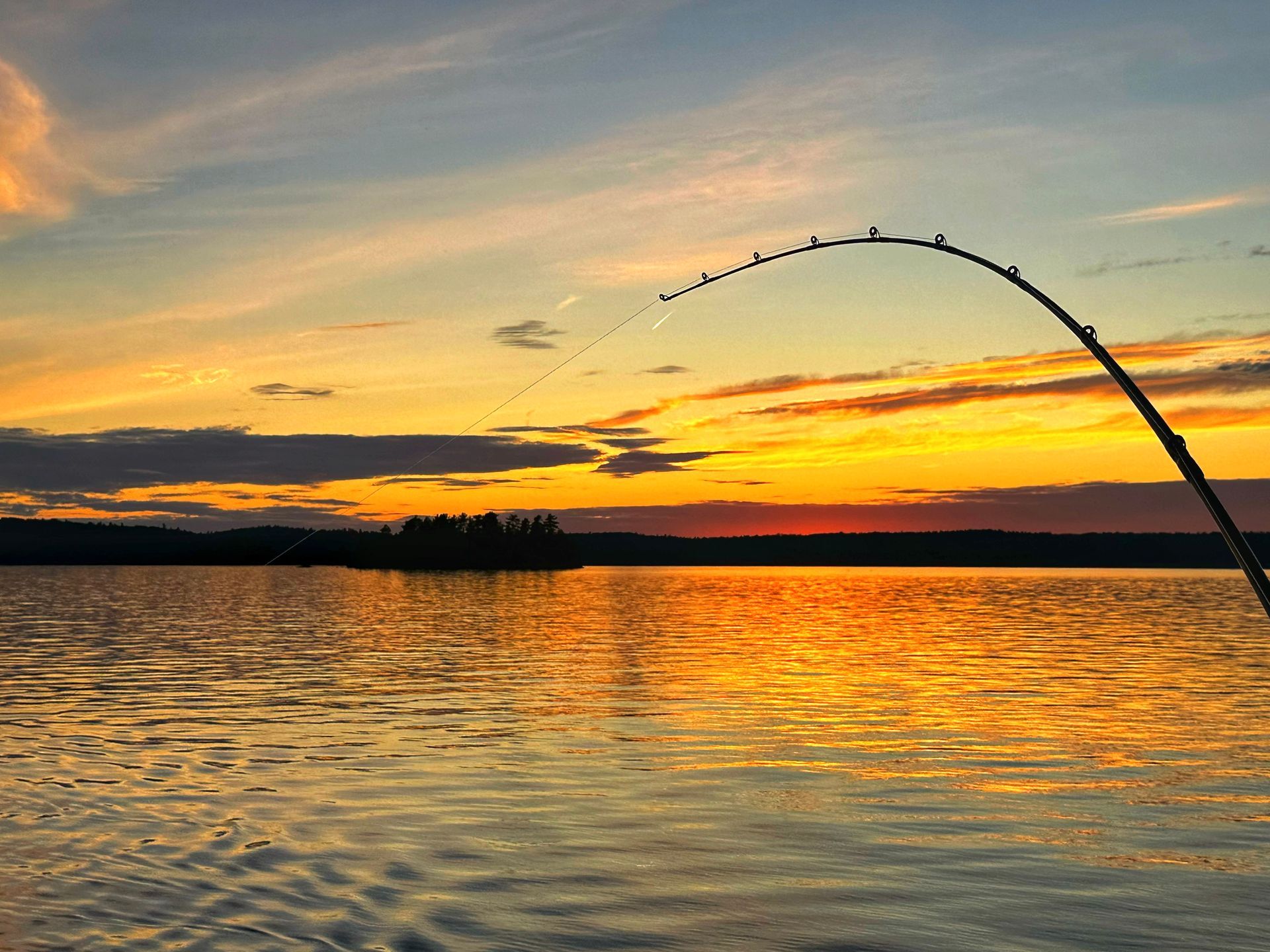 Fishing rod over rippling water at sunset, with orange and pink sky reflecting on the lake
