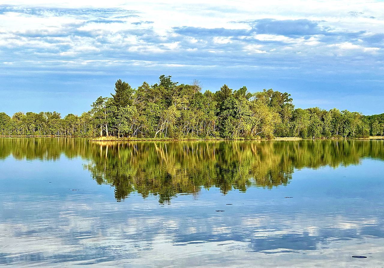 Tropical island reflected in calm blue water under a partly cloudy sky