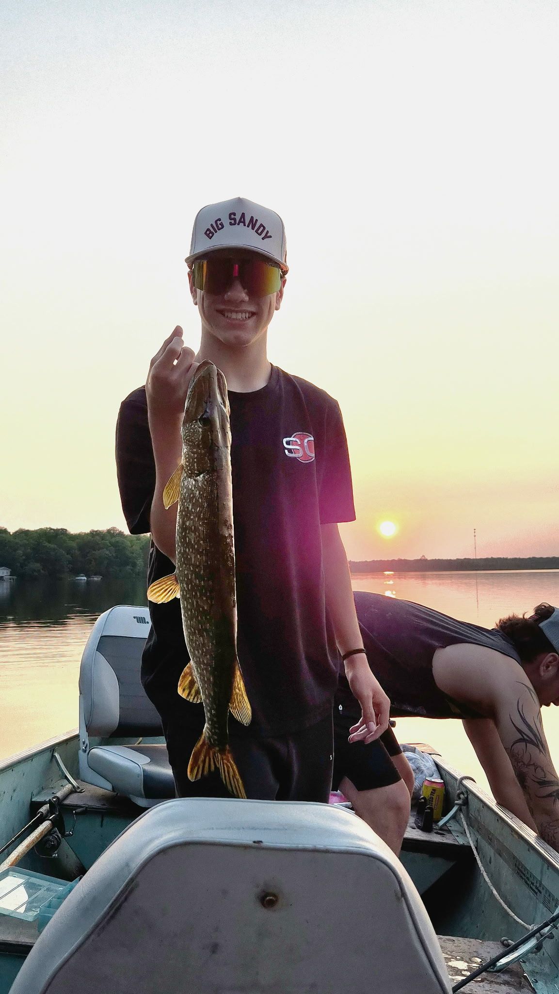 Person on a boat holding a large fish at sunset on the water.