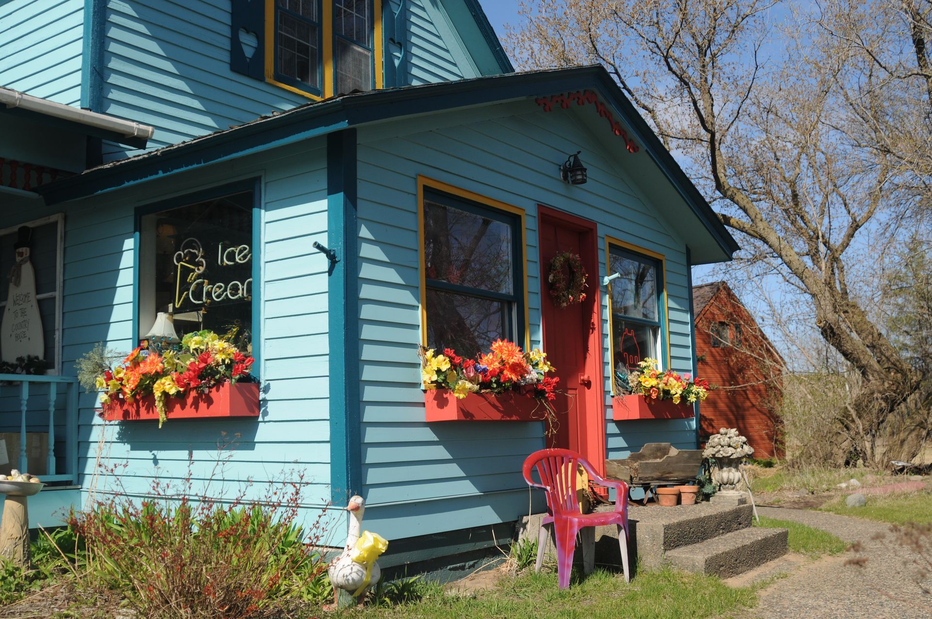 Blue cottage with red door, flower boxes, and a porch in a sunny yard