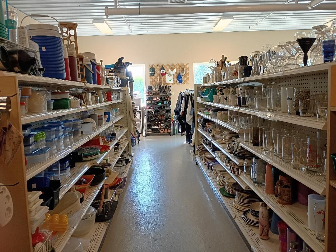 A narrow thrift store aisle lined with shelves of assorted household goods and glassware.