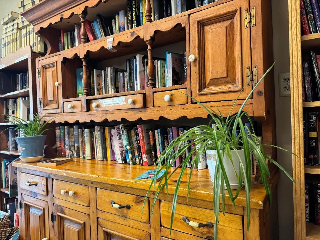 Wooden hutch with shelves of books and a green potted plant on the sideboard.