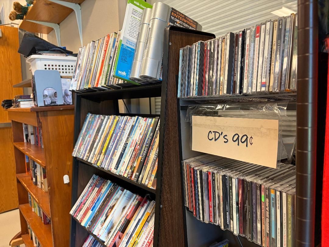 Metal shelves packed with CDs in a shop, with a handwritten “CD’s 99¢” sign.