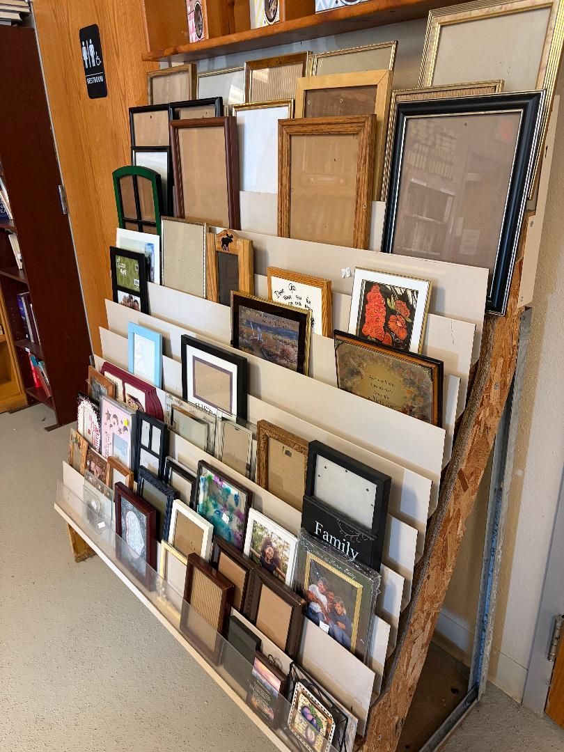 Wall display of assorted empty picture frames in various sizes and colors leaning in rows