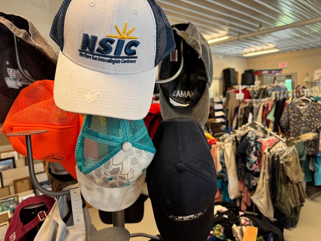 Display of baseball caps in a store, including a white NSIC cap and a black ANA cap