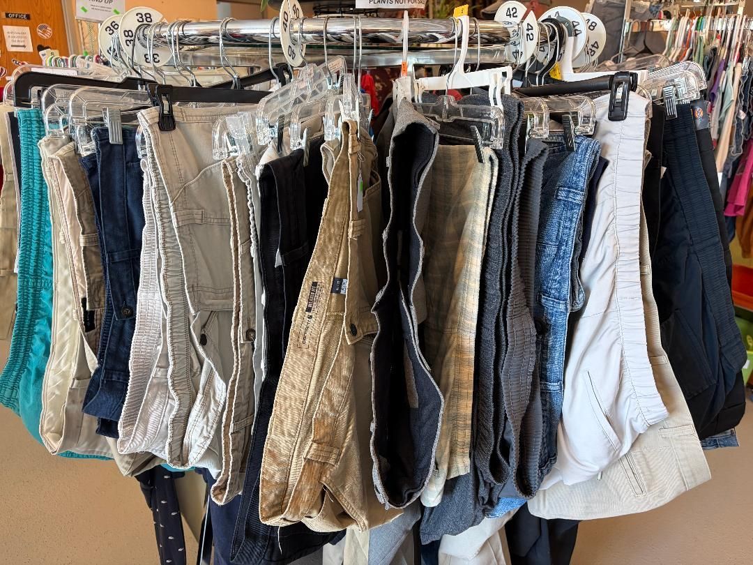 Racks of assorted hanging pants and jeans in a clothing store, in neutral and blue tones