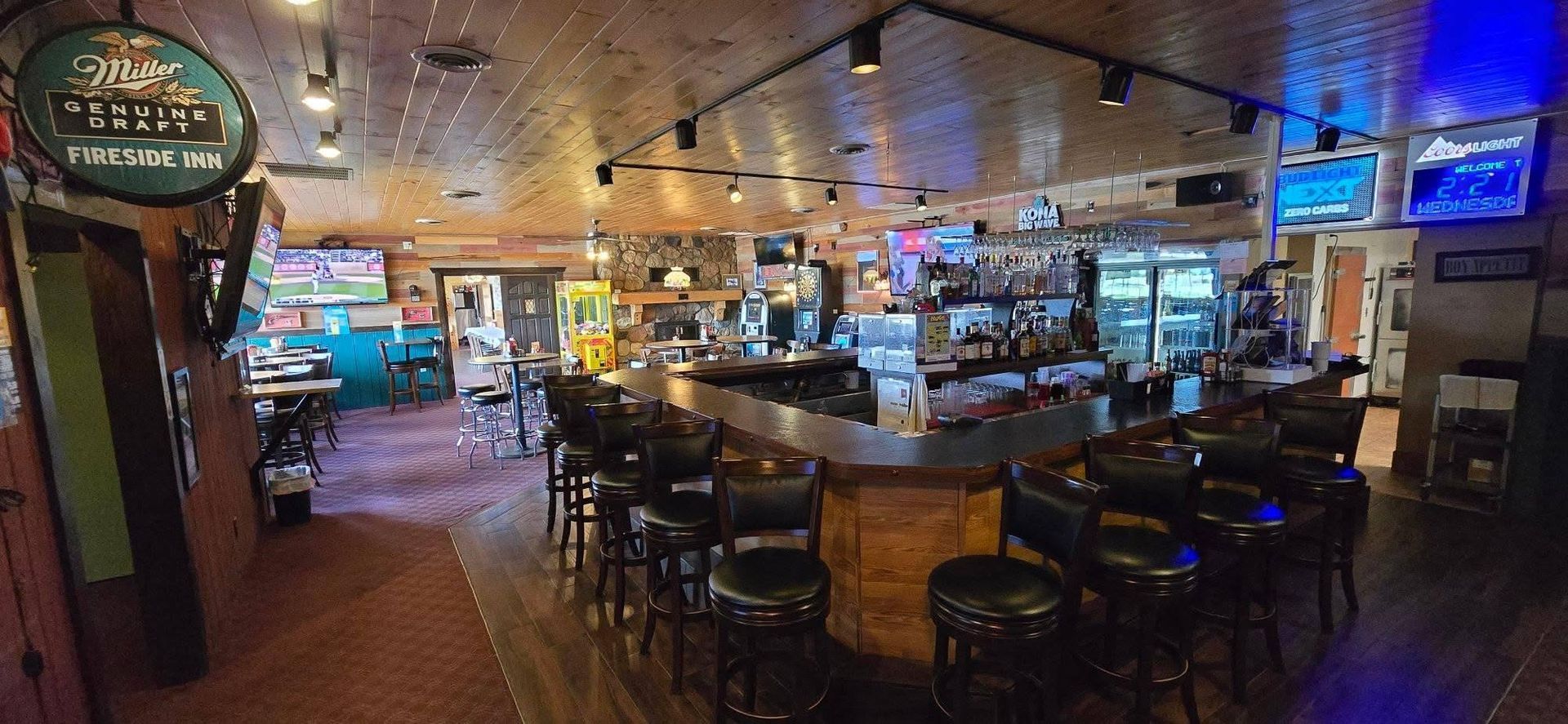 Dimly lit sports bar with tables, stools, neon signs, and TV screens in the background