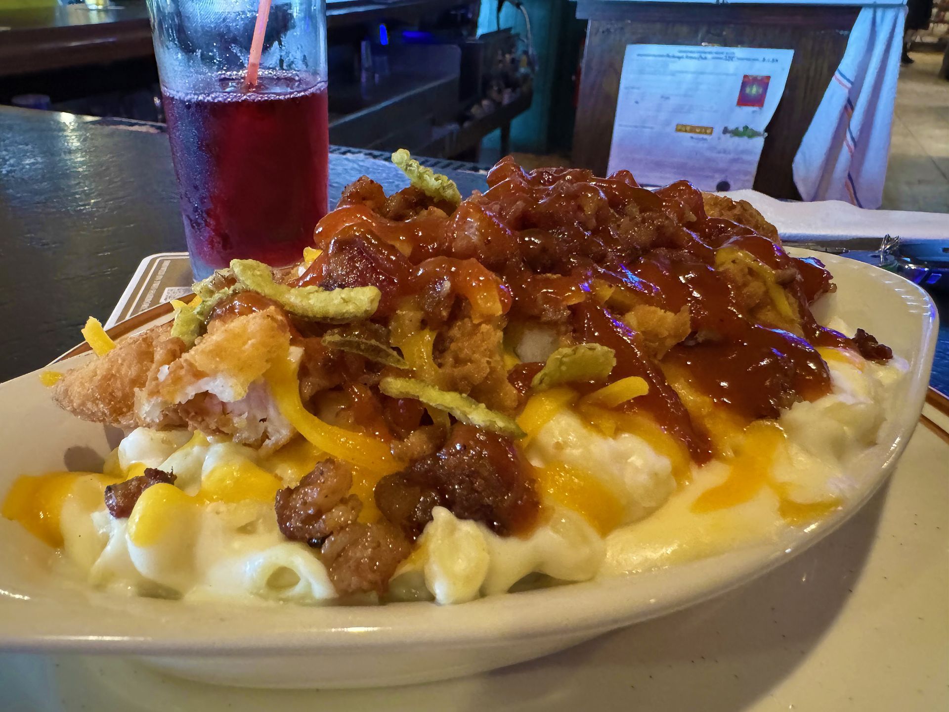 Plate of loaded fries topped with melted cheese and chili, beside a red drink in a restaurant