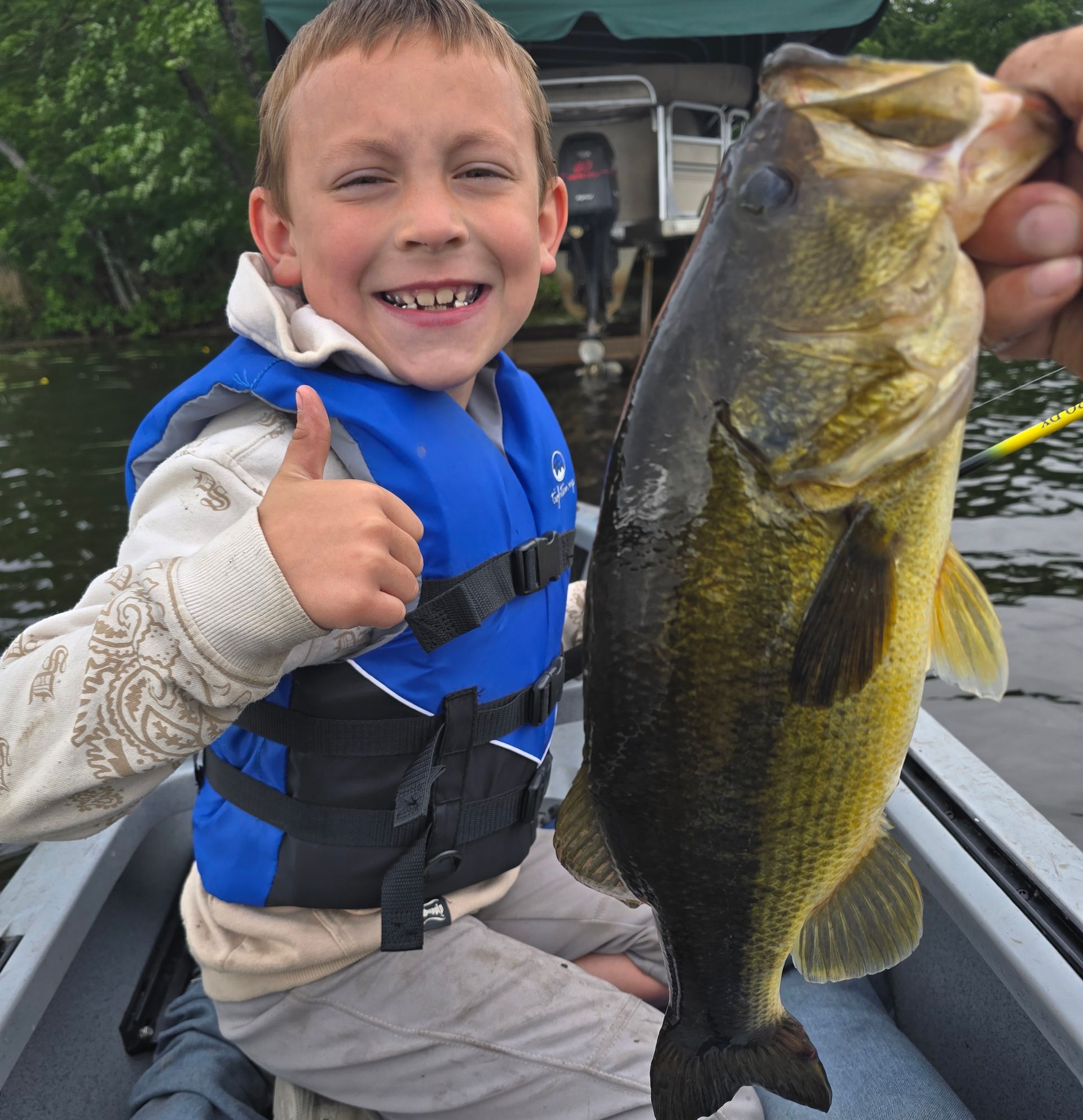 Smiling child in a blue life vest holding up a large fish on a boat