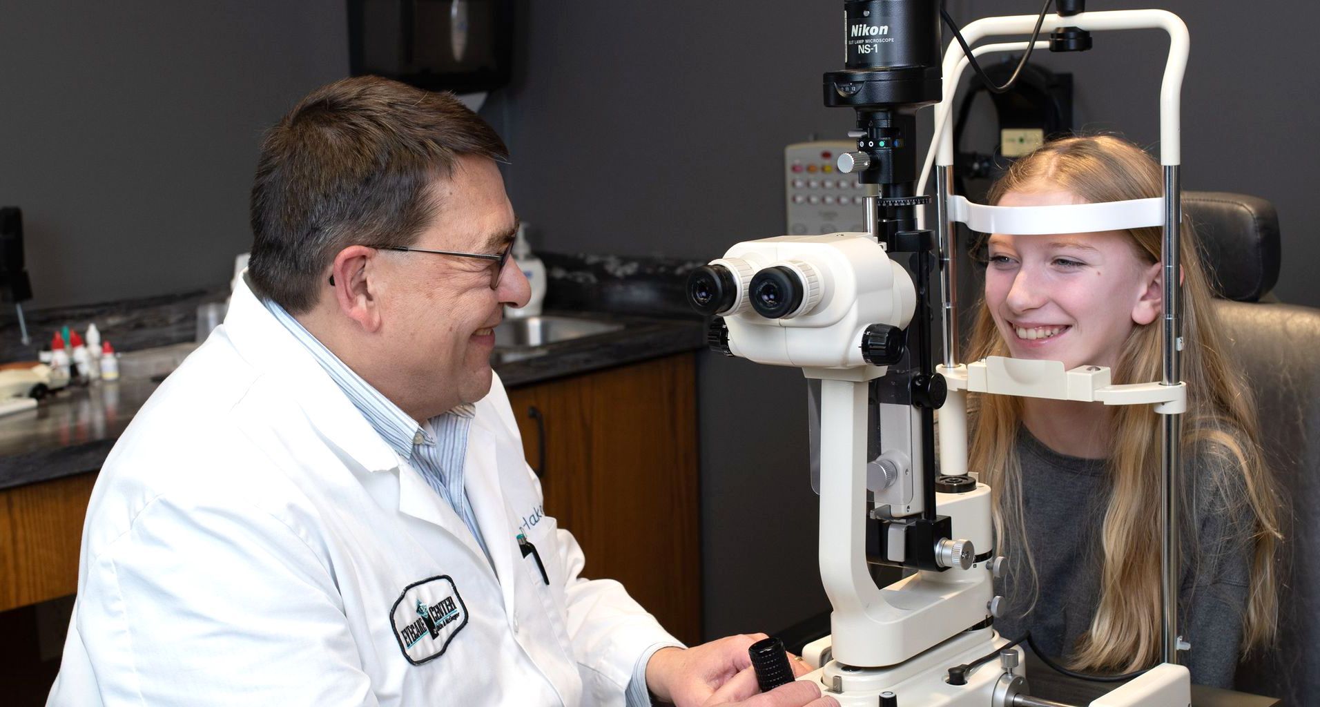 Eye exam with doctor and smiling patient using a slit lamp microscope.