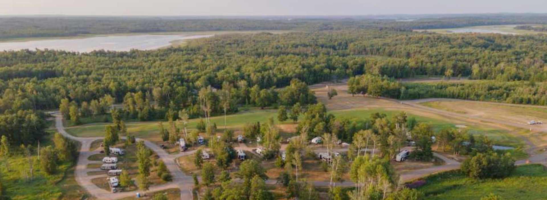 Aerial view of a suburban neighborhood surrounded by dense green forest and a river in the distance