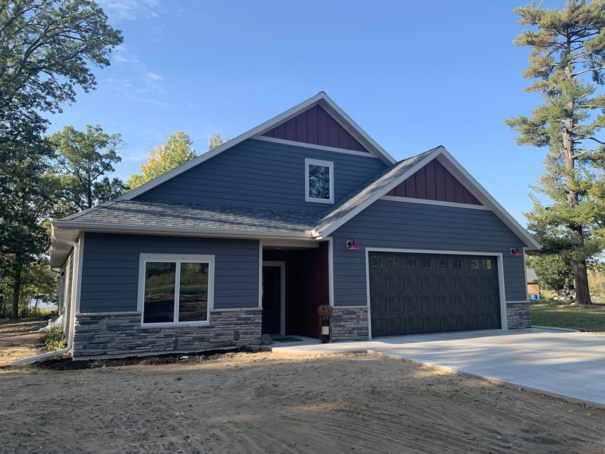 Gray house with stone accents, double garage, and driveway under a clear blue sky