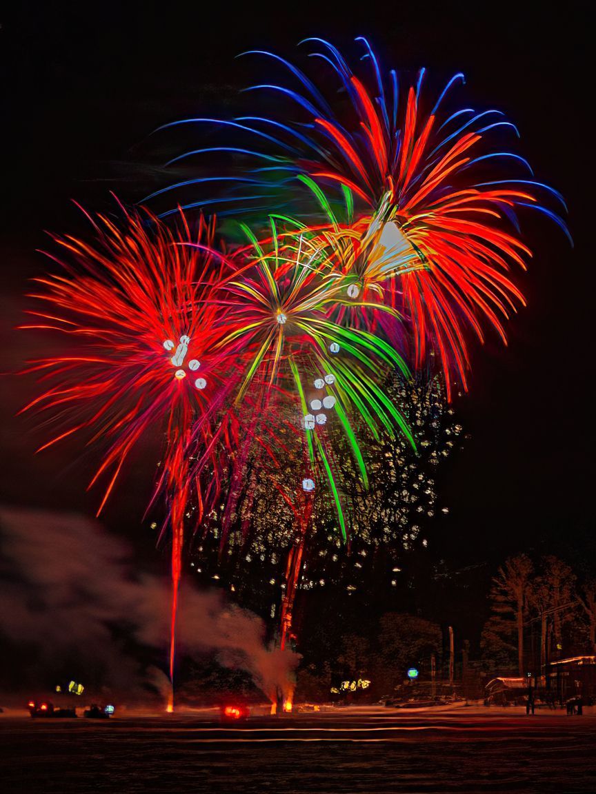 Colorful fireworks bursting in the night sky above a dark field with smoke below