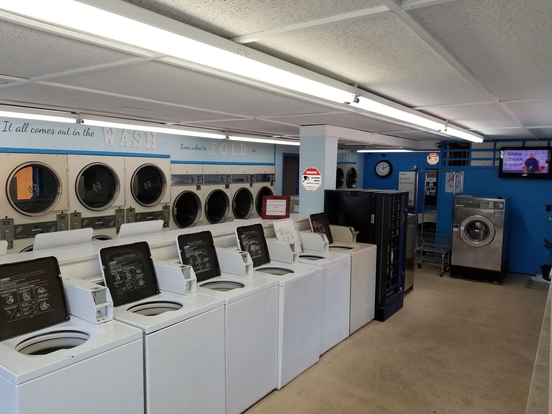 Laundry room with rows of washing machines and dryers in a bright, blue-walled laundromat