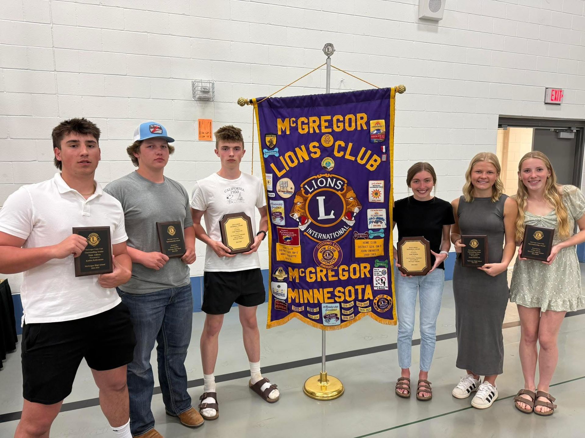 Six students holding awards in front of a McGregor Lions Club banner in a gymnasium