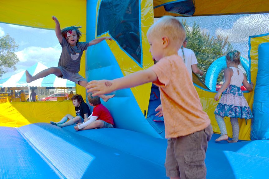 Children playing on a colorful inflatable bounce house at a sunny outdoor event.