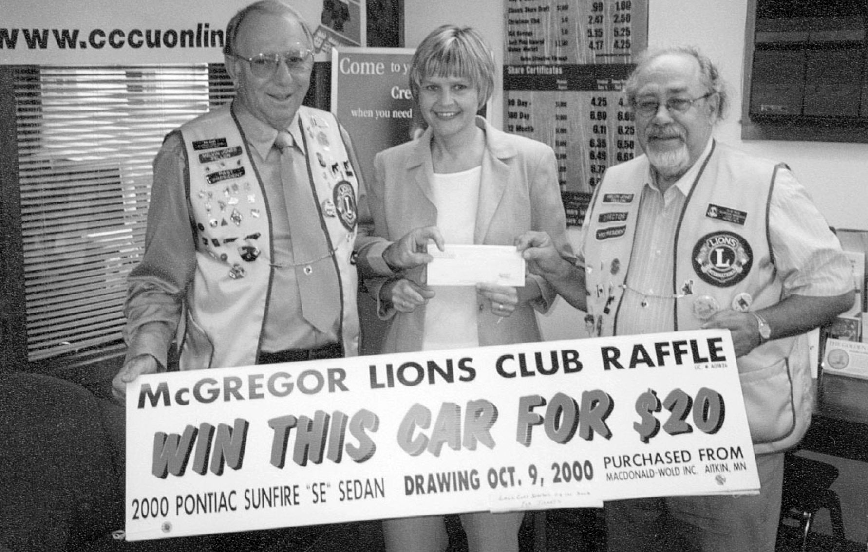 Three people hold a raffle sign reading “Win this car for $20” at McGregor Lions Club.