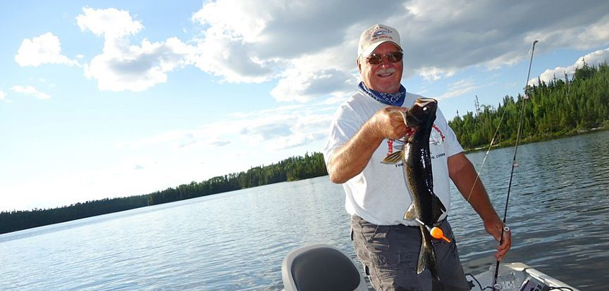 Man holding a fish on a boat on a lake under a bright blue sky