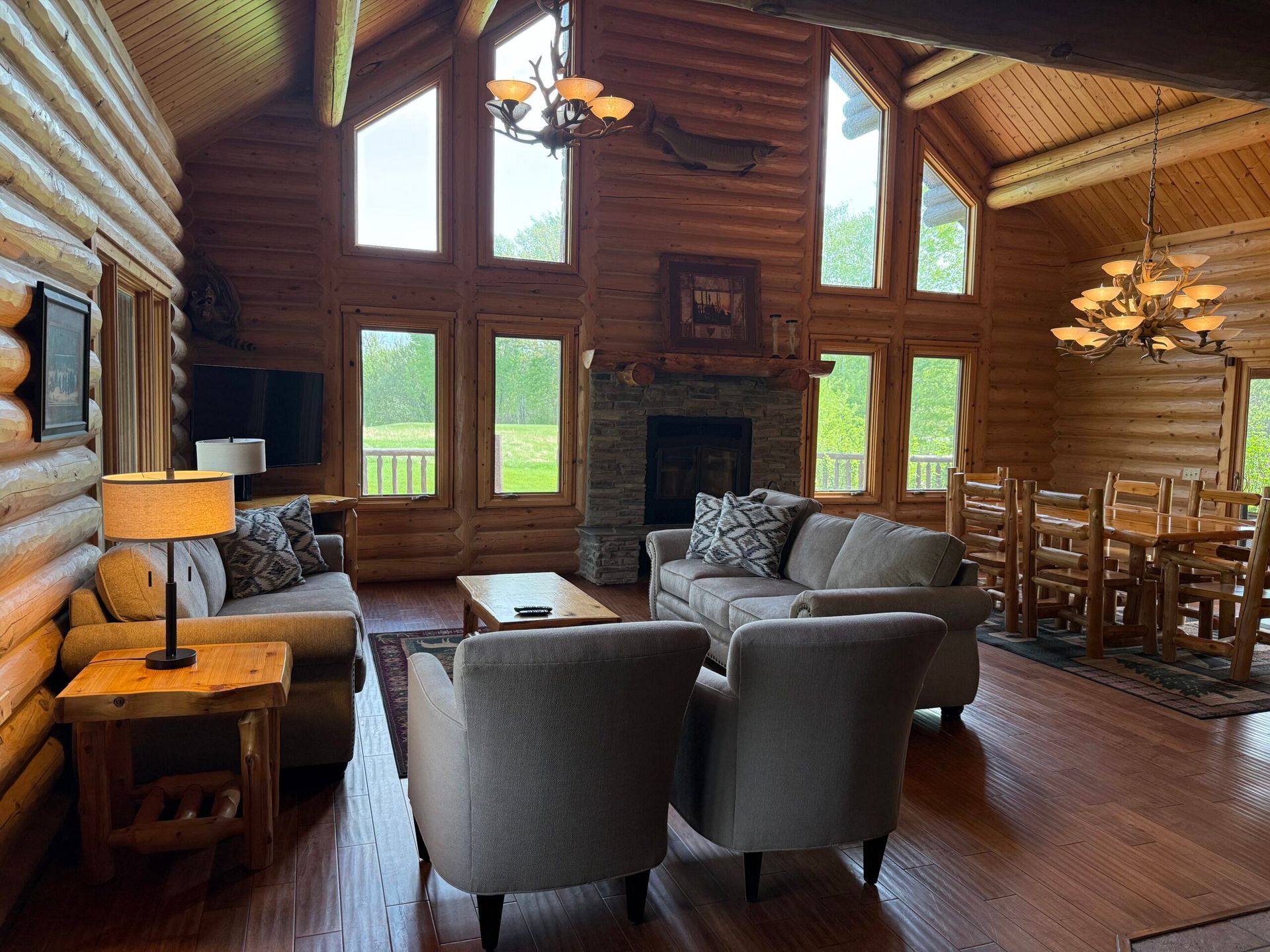 Cozy log cabin living room with stone fireplace, large windows, and gray armchairs around a coffee table