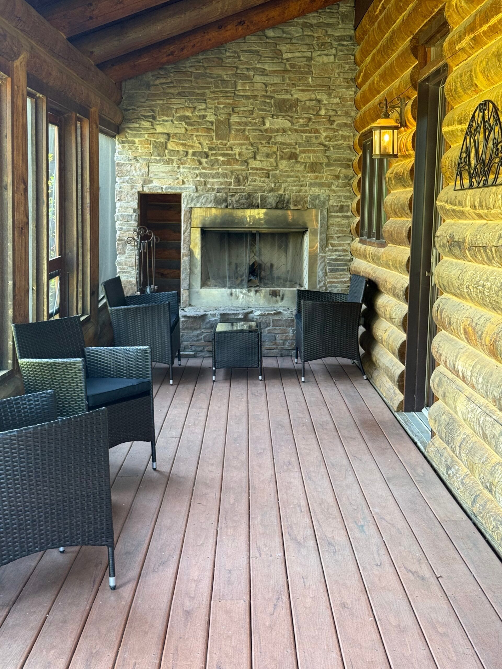 Covered stone porch with wicker chairs, wooden floor, and a fireplace at the far end