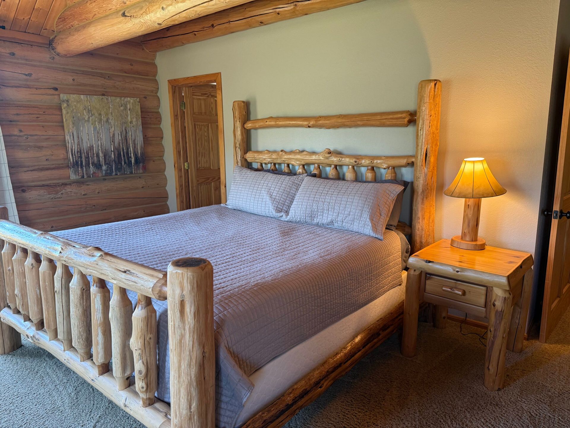 Rustic log bed with gray bedding and bedside lamp in a cozy wood-paneled bedroom