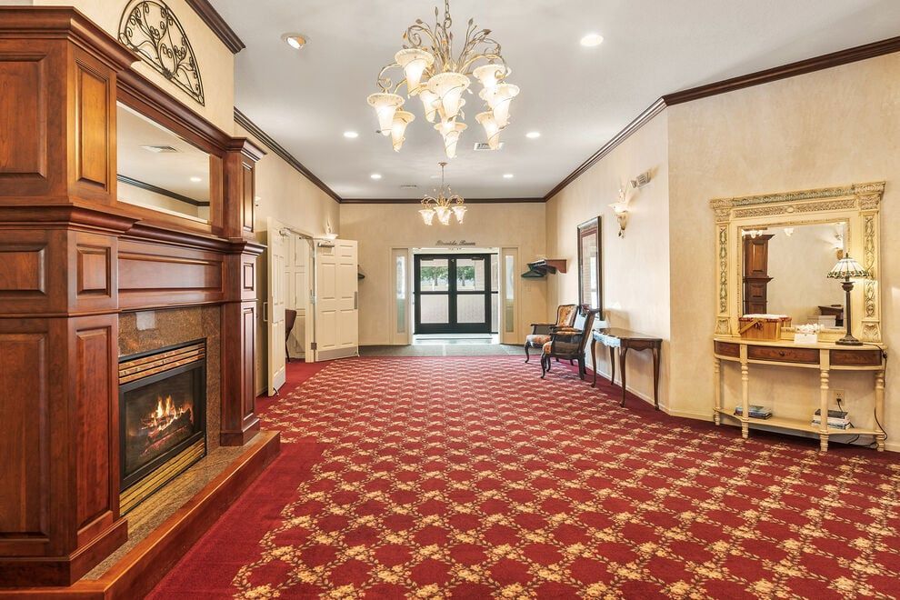 Elegant hotel lobby with red patterned carpet, chandelier, wooden fireplace, and ornate mirror wall
