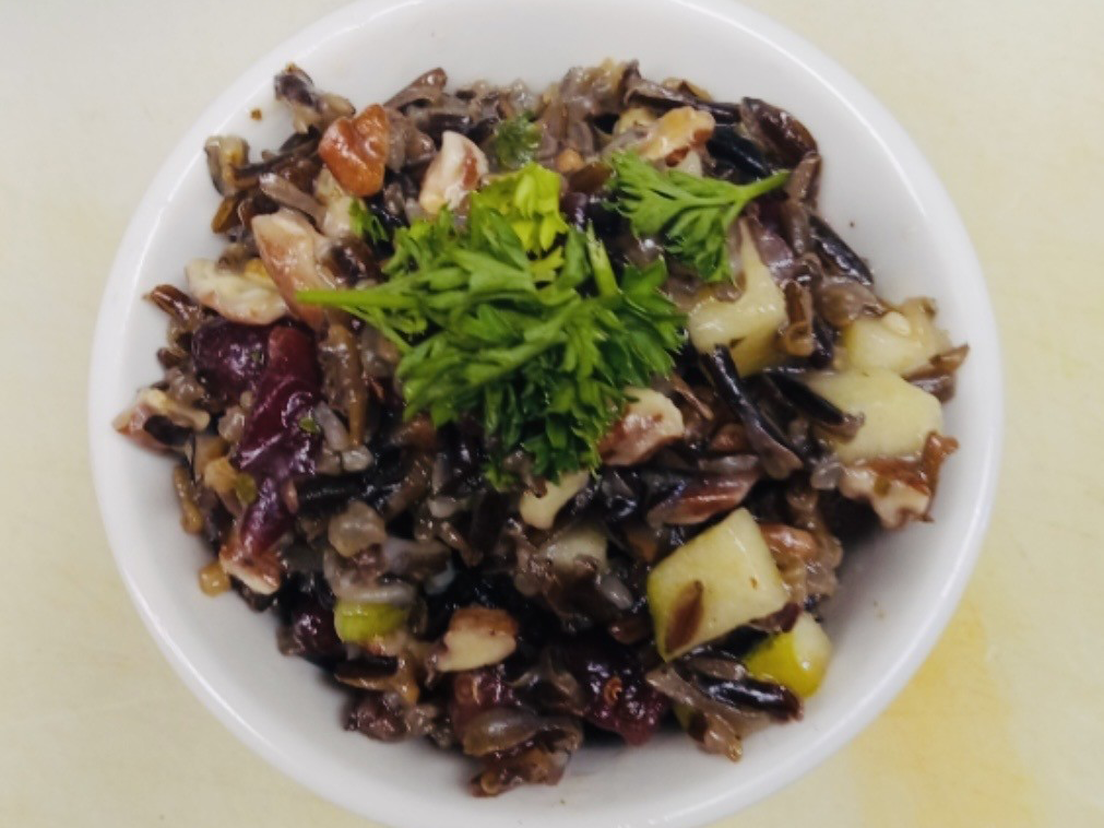 Bowl of wild rice, diced vegetables, and fresh green herbs on top