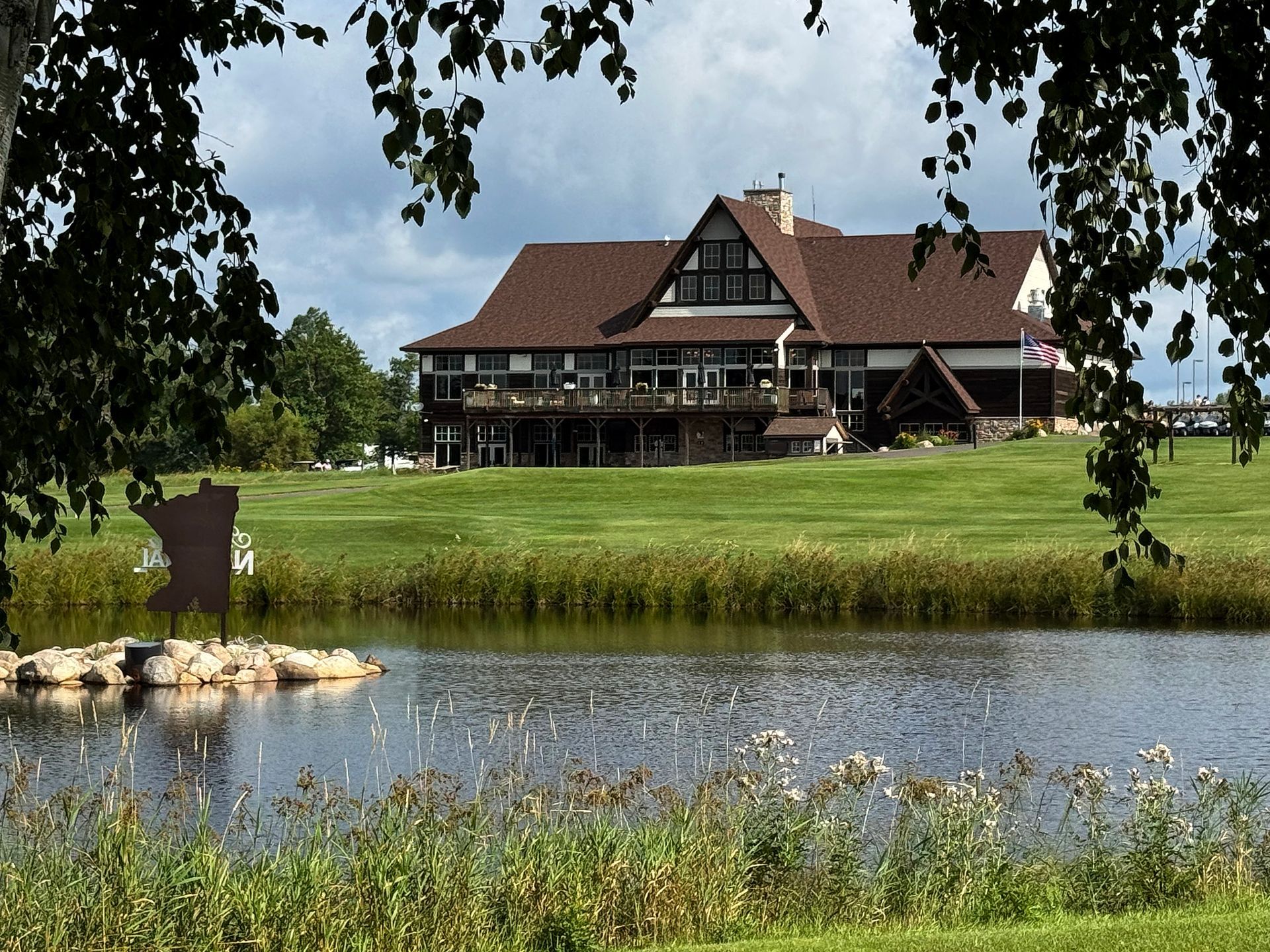 Lakeside lodge with red roofs and green lawn, framed by trees under a clear sky.