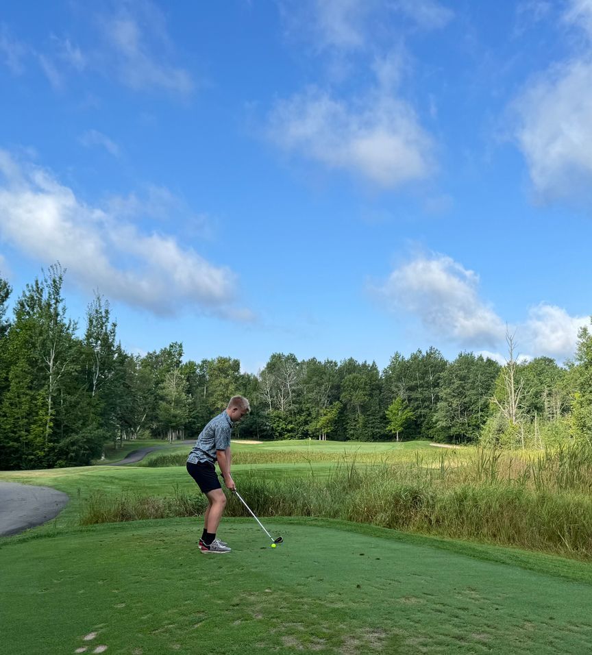 Golfer preparing to swing on a green tee box beside a pond under a blue sky