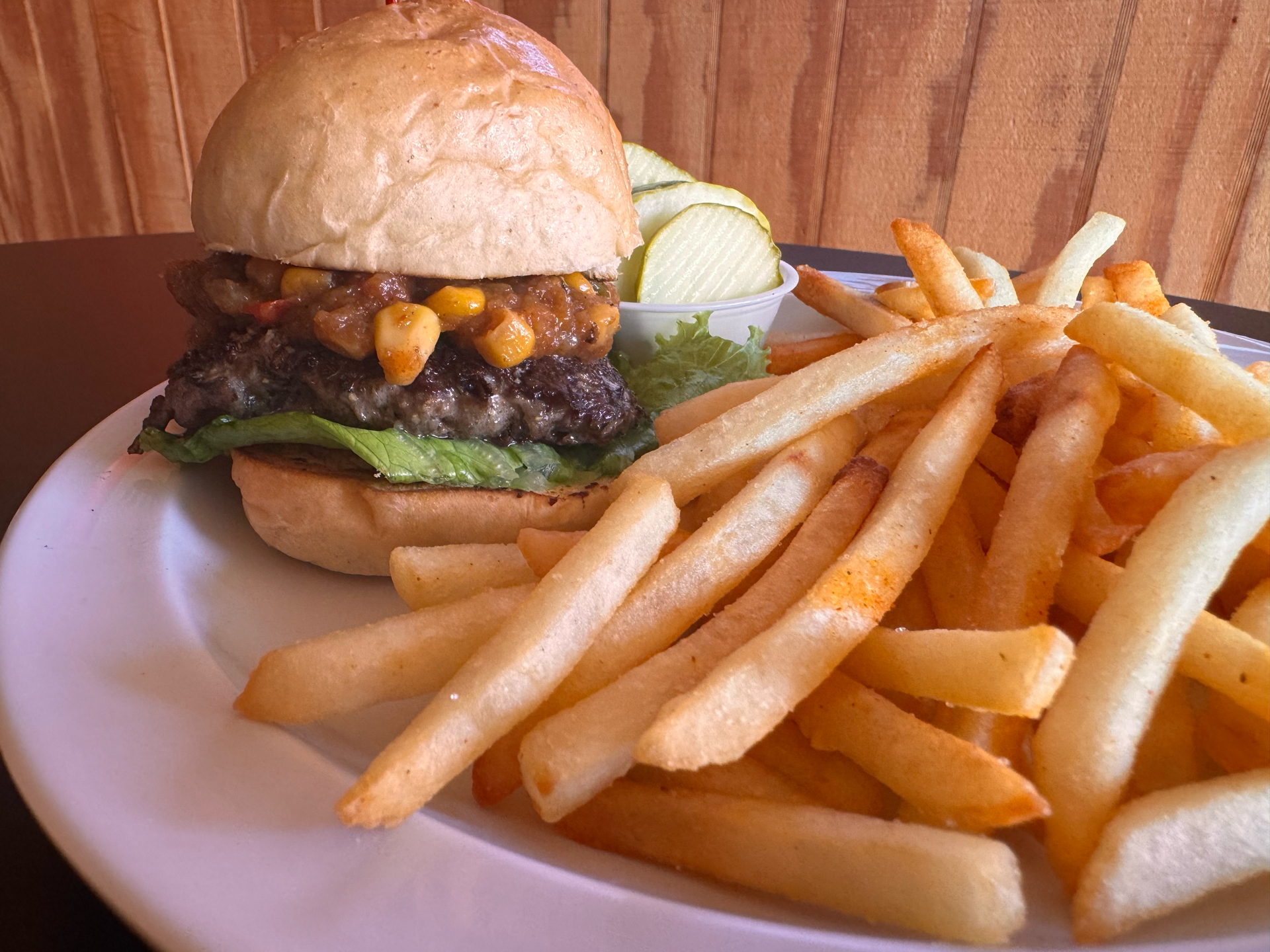 Wild rice burner with lettuce, corn relish, pickles, and French fries on a white plate