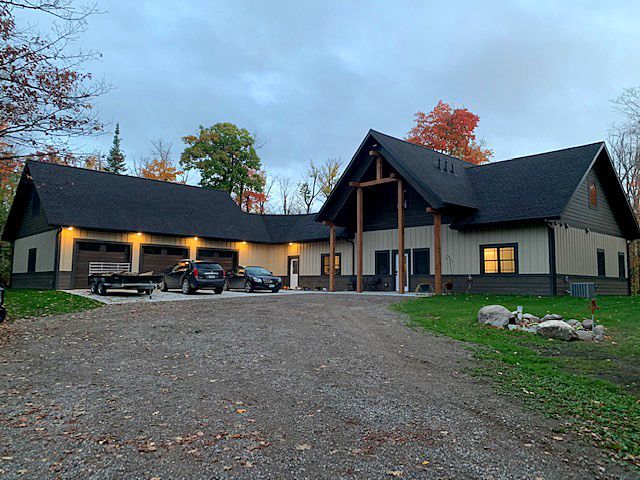 Large beige lodge with dark roofs at dusk, warm lights on, parked cars in front of a gravel driveway.