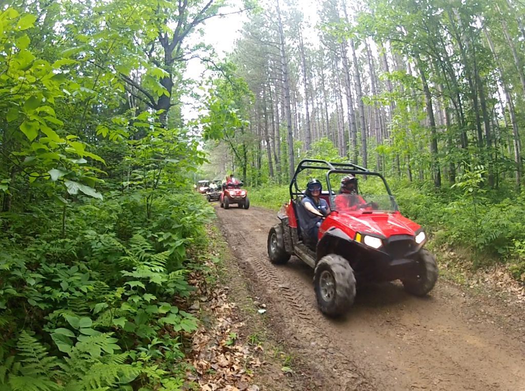 Two red off-road buggies driving on a muddy forest trail
