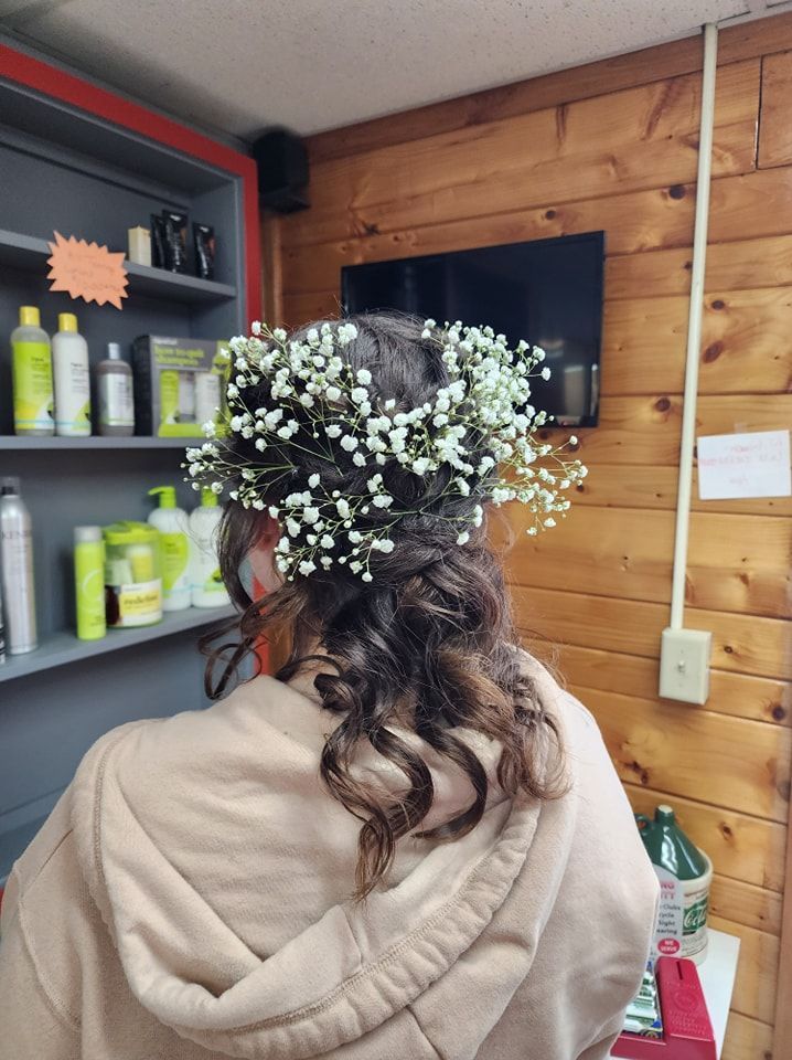 Person with floral hairpiece in a wood-paneled salon, seen from behind, wearing a beige hoodie.