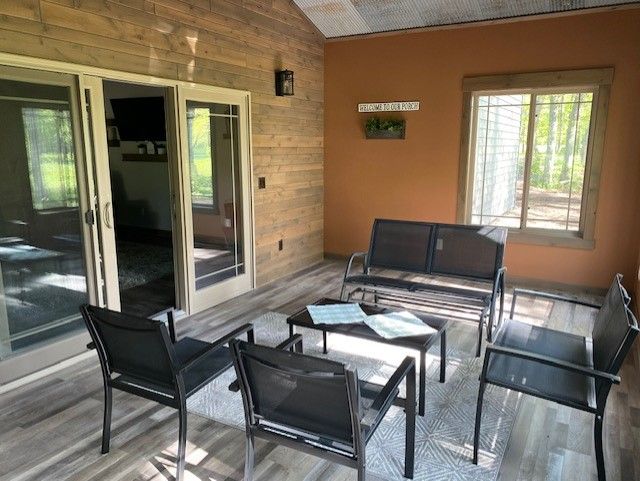 Covered porch seating area with black chairs and glass tables beside sliding doors and a window