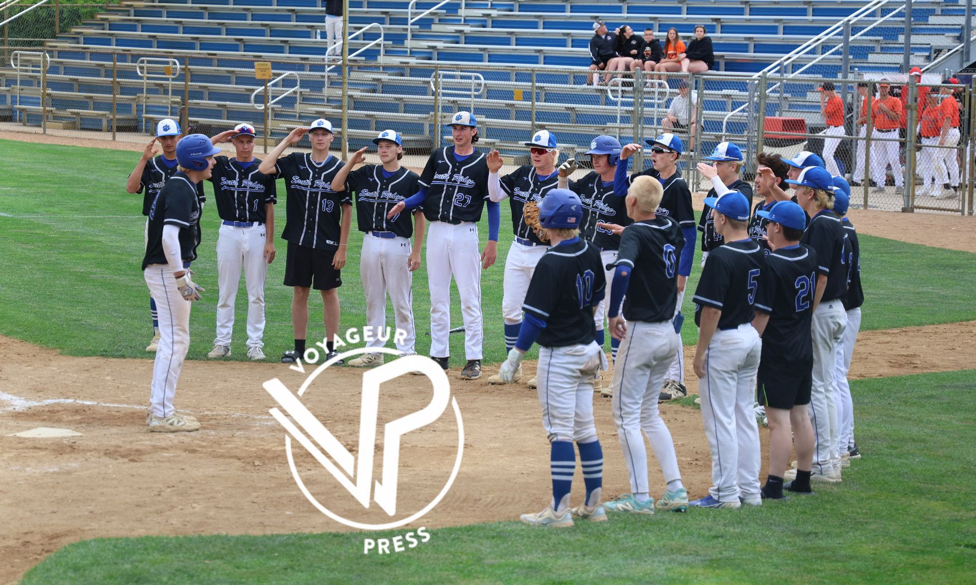 Baseball team in navy jerseys and white pants standing on the field during practice, with stadium bleachers behind them