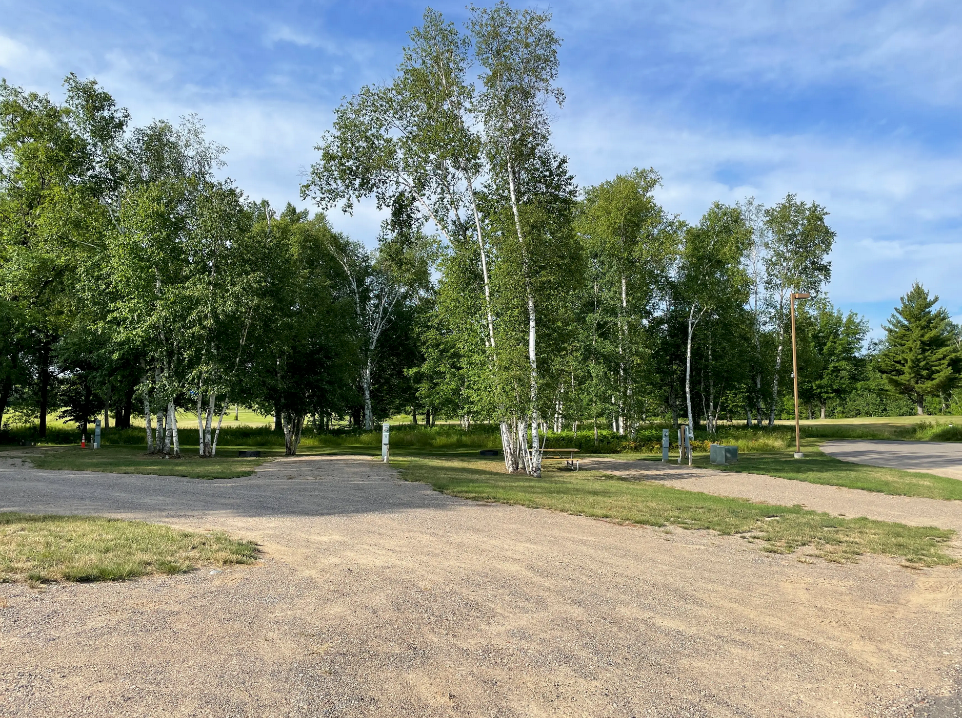 Gravel path beside green trees in a sunny park under a blue sky