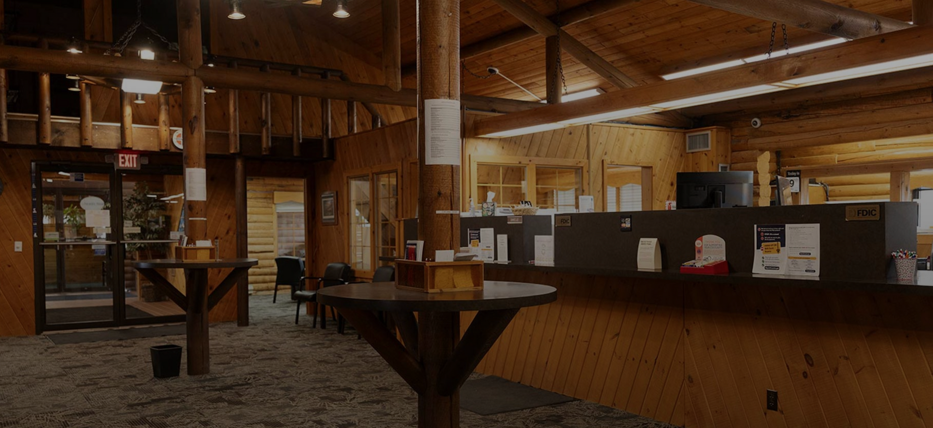 Wooden lodge lobby with a fireplace, bar counter, and small tables under warm lighting