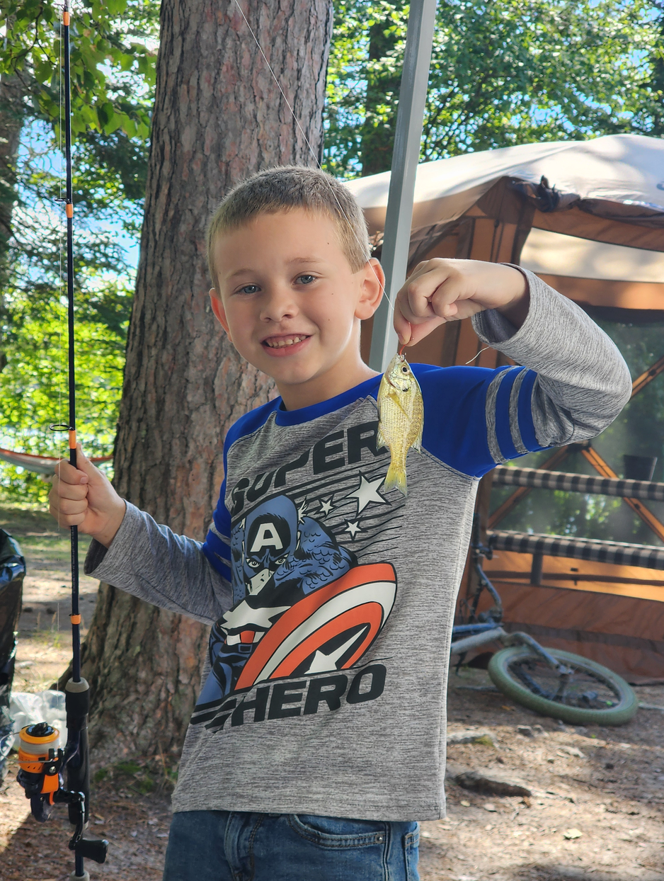 Boy smiling on a backyard swing, wearing a gray Avengers shirt and holding the ropes.