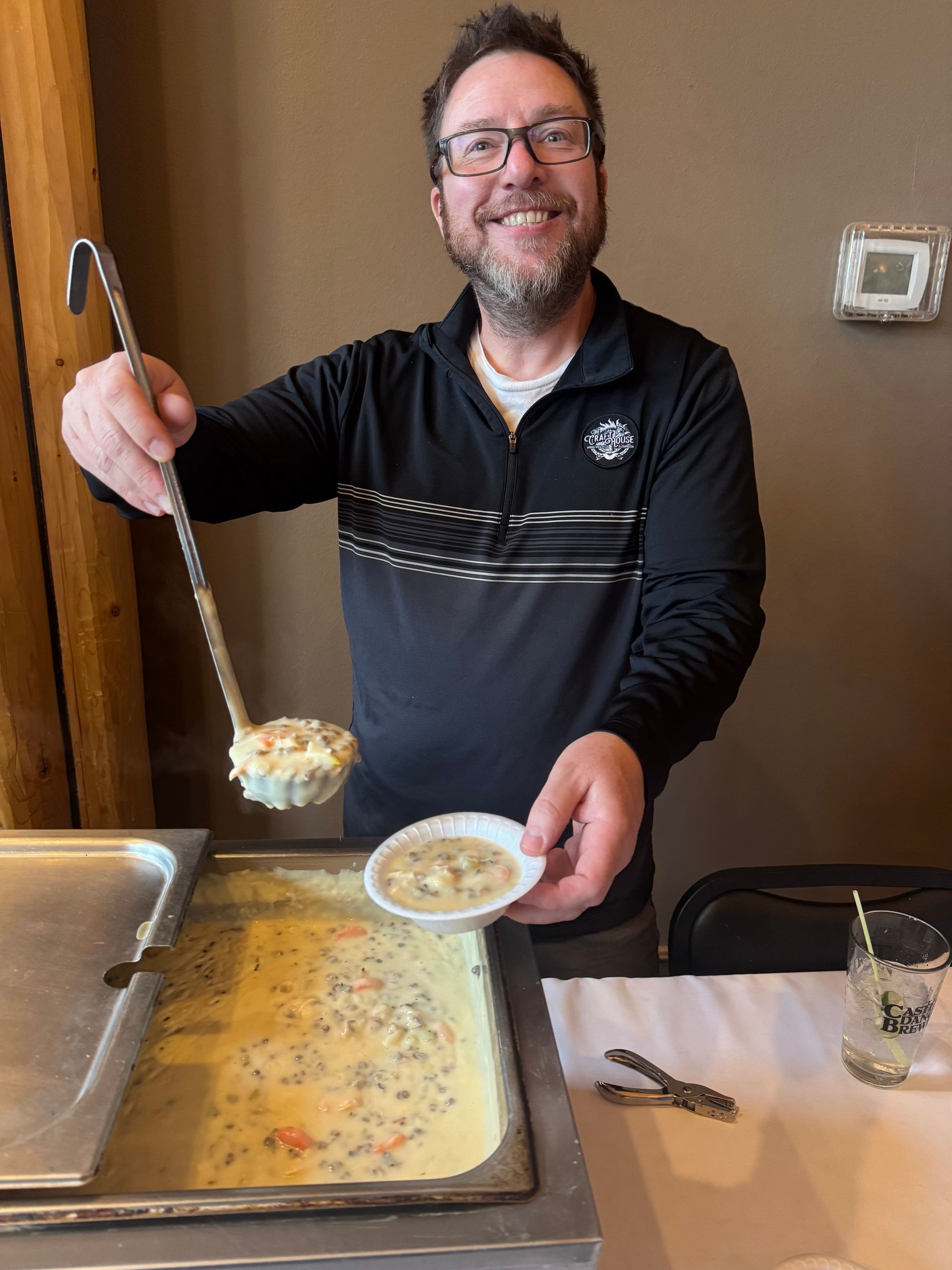 Man serving soup from a large pot into a bowl at a kitchen counter