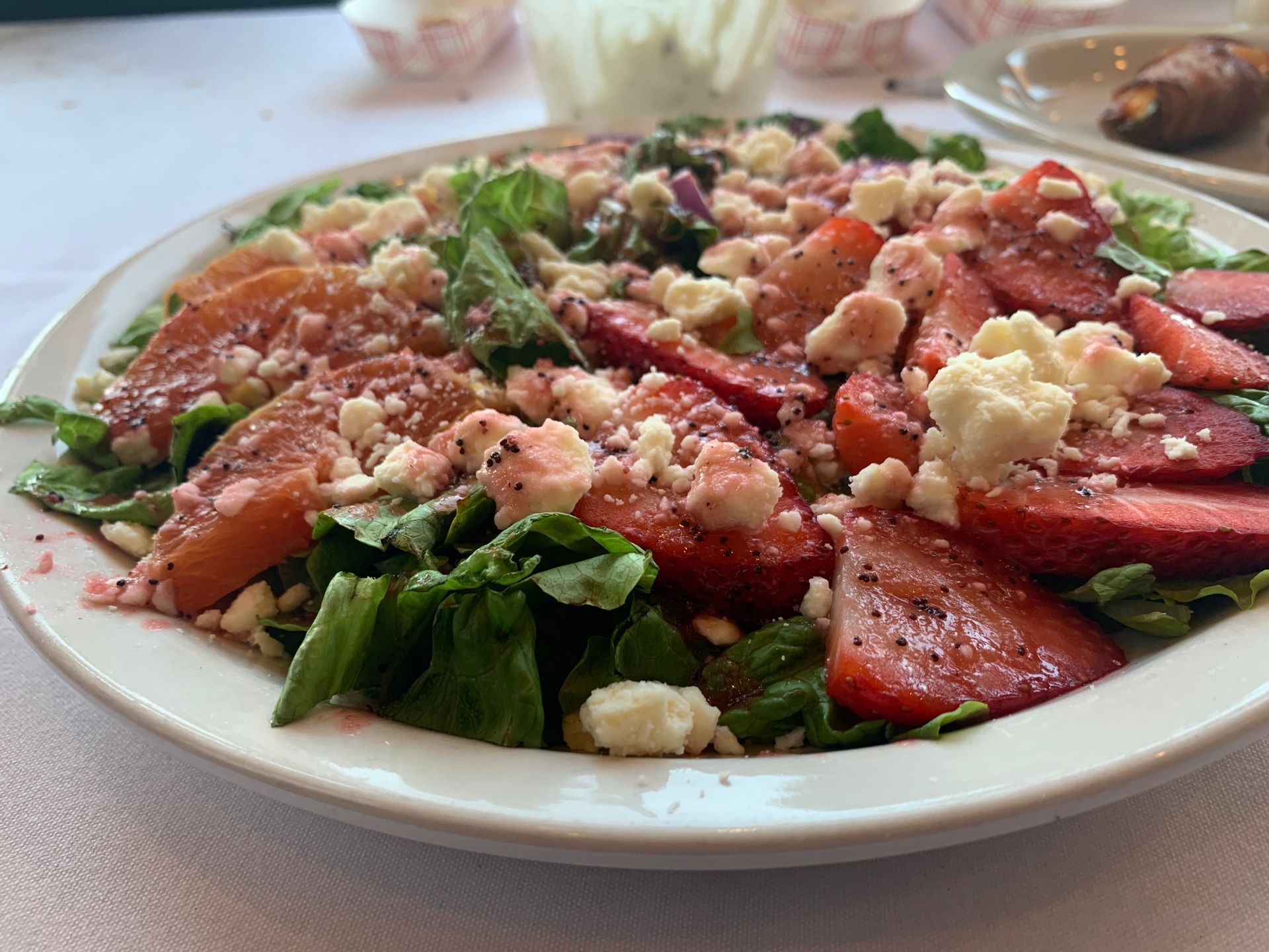 Salad with strawberries, crumbled cheese, and leafy greens on a white plate