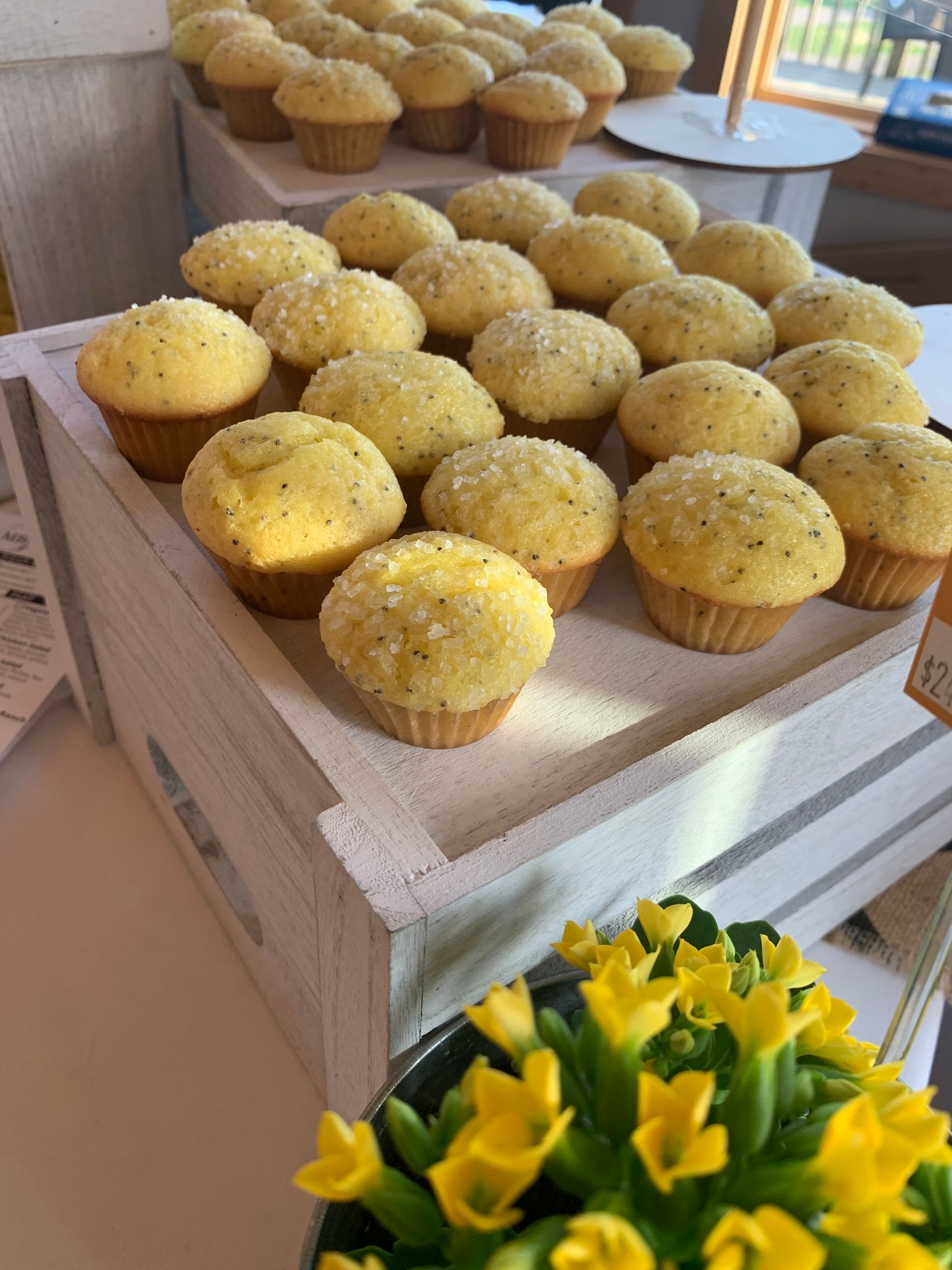 Tray of yellow muffins on a rustic white stand, with a bouquet of yellow flowers in the foreground.